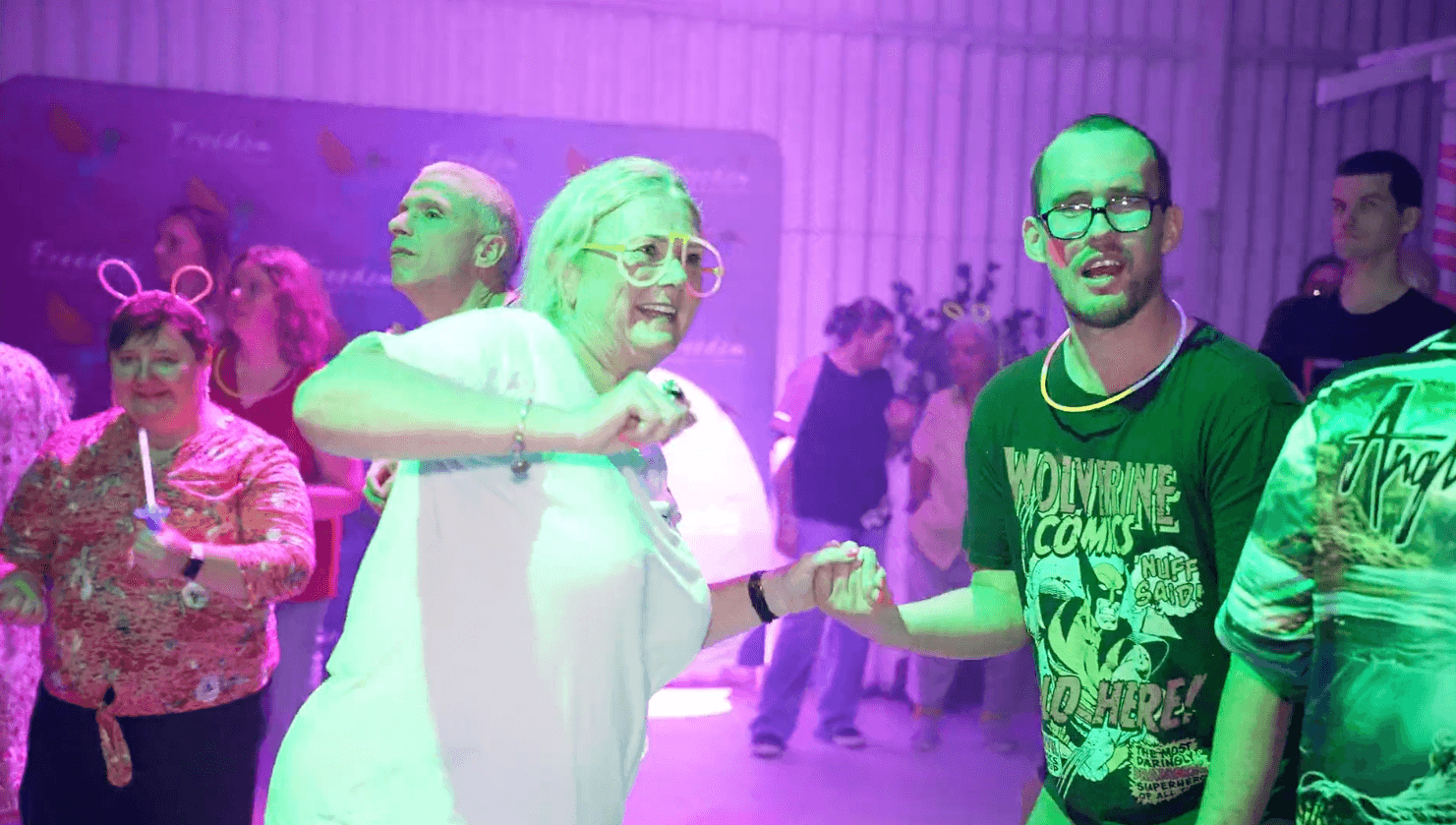 Two friends dancing hand in hand under neon lights at Freedom's glow party